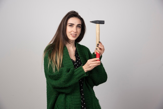 Pensive woman holding hammer in hands on a gray background.