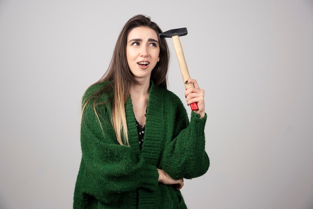 Pensive woman holding hammer in hands on a gray background.