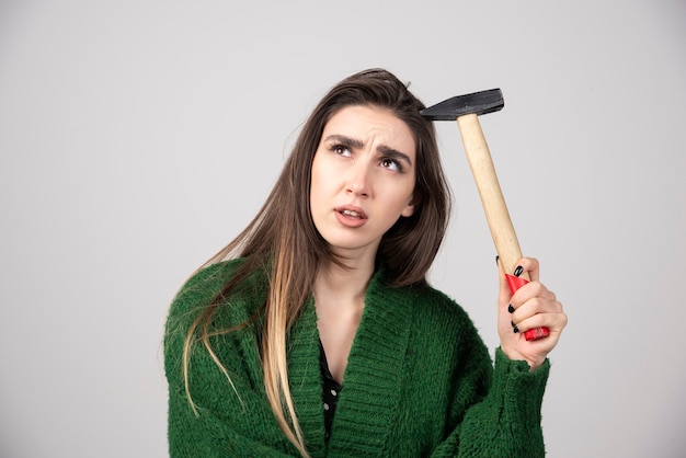 Pensive woman holding hammer in hands on a gray background.