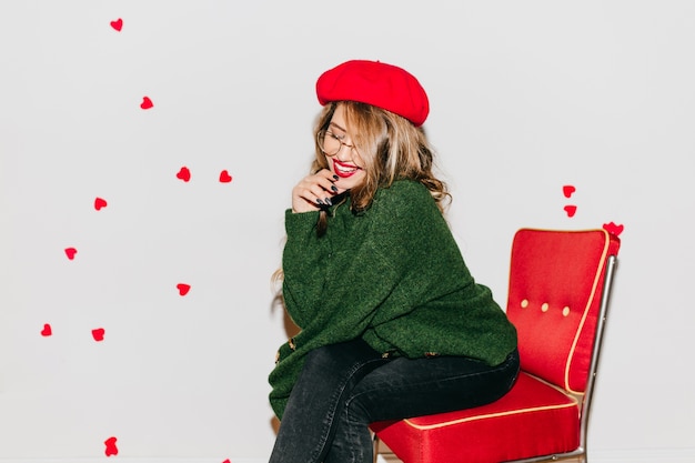 Free Photo pensive woman with shiny hair sitting on red chair and smiling