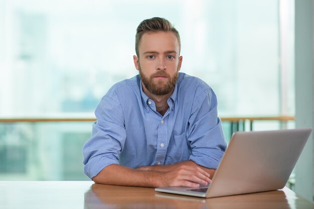 Pensive Young Man Working on Laptop at Cafe Table