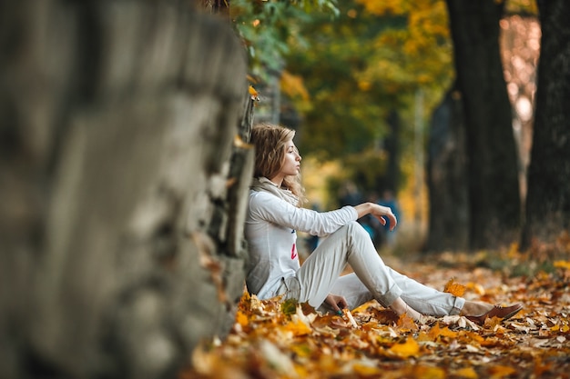 Free photo pensive young woman sitting on dry leaves