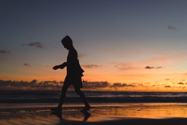 people on the beach at sunset. the girl is jumping against the backdrop of the setting sun.