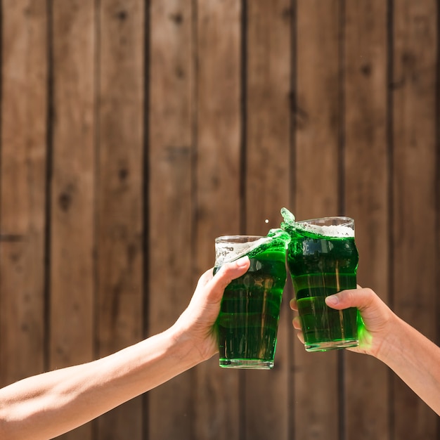 People clanging glasses of green drink near wooden wall