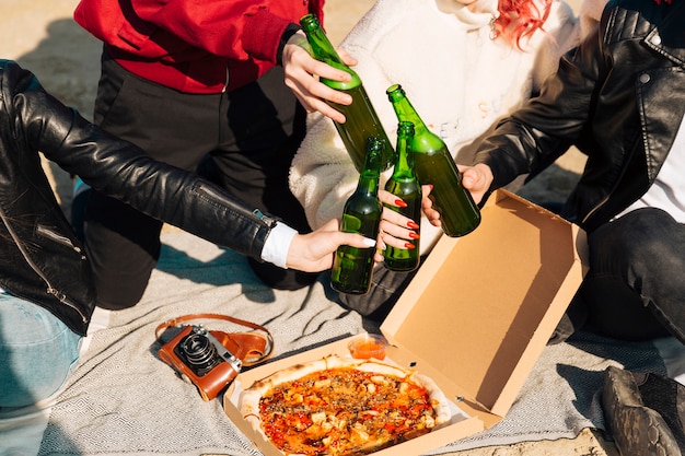 People clinking beer bottles on picnic