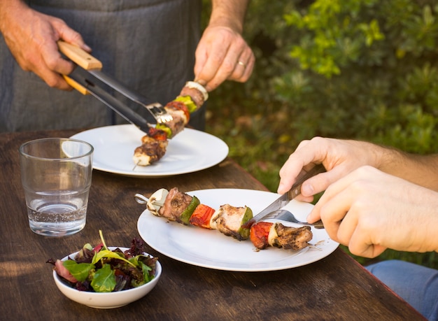 People eating cooked barbecue in plates on table 