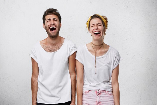 People, facial expressions and body language concept. Young female and her boyfriend laughing with widely opened mouth and closed eyes