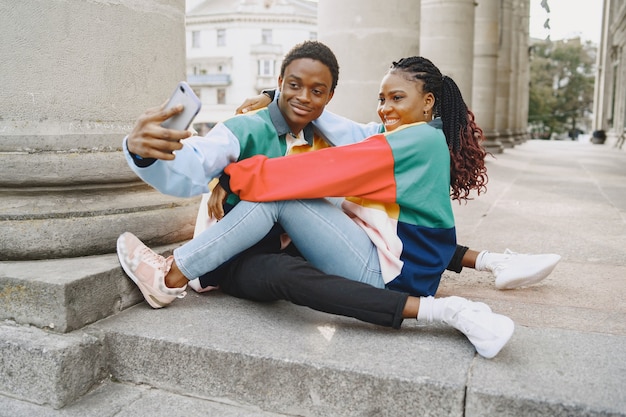 People in identifical clothes. African couple in autumn city. People sitting and uses phone.