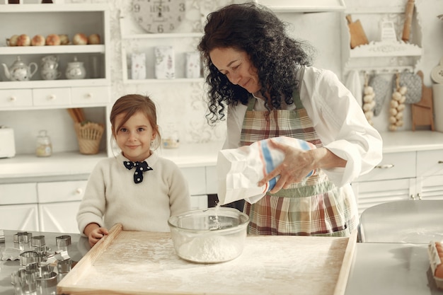 People in a kitchen. Grandmother with little daughter. Adult woman teach little girl to cook.