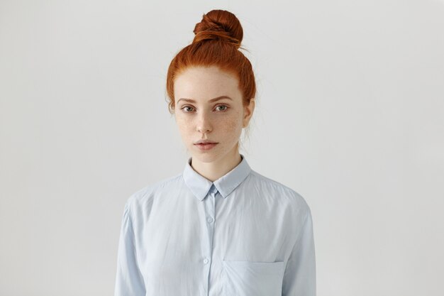 People and lifestyle. Attractive European student woman with freckles and ginger hair in bun wearing formal shirt, ready for college