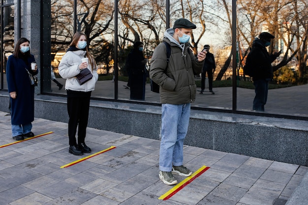 Free photo people in line waiting behind social distance stripe