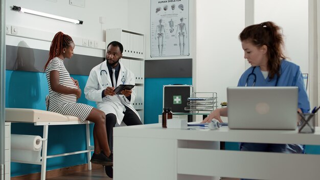 People meeting in medical office to talk about pregnancy and childbirth, pregnant woman asking for advice from obstetrician. Medic having conversation with expectant patient and taking notes.