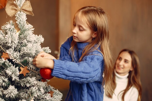 People reparing for Christmas. Mother playing with her daughter. Family is resting in a festive room. Child in a blue sweater.