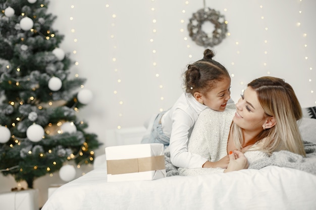 People reparing for Christmas. Mother playing with her daughter. Family is resting in a festive room. Child in a sweater sweater.