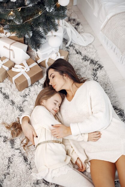 People reparing for Christmas. Mother playing with her daughter. Family sitting by the Christmass tree. Little girl in a white dress.