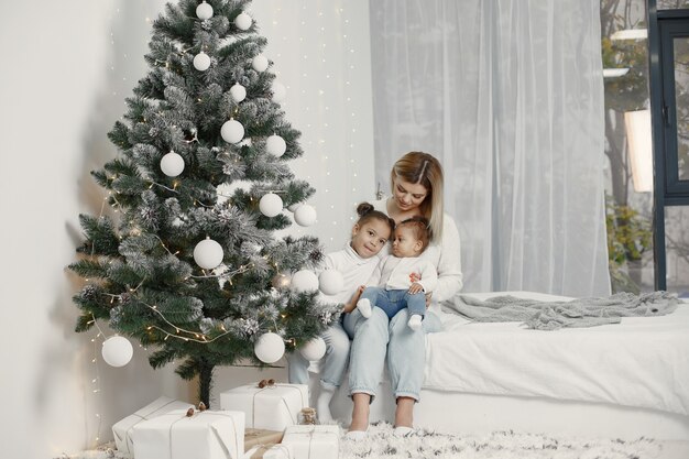 People reparing for Christmas. Mother playing with her daughters. Family is resting in a festive room. Child in a sweater sweater.