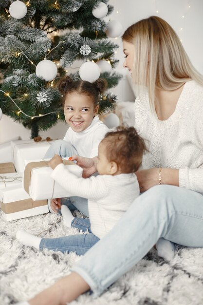 People reparing for Christmas. Mother playing with her daughters. Family is resting in a festive room. Child in a sweater sweater.