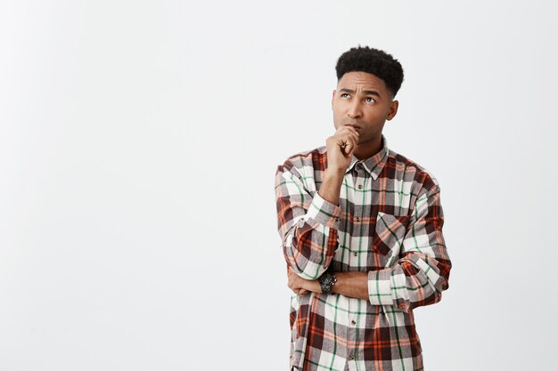 People's emotions. Close up portrait of young attractive dark-skinned men with curly hair in casual shirt holding hand near mouth with thoughtful expression, being curious about film he saw.