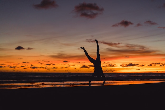 Free photo people on the shore of the ocean at sunset. man jumps against the backdrop of the setting sun.