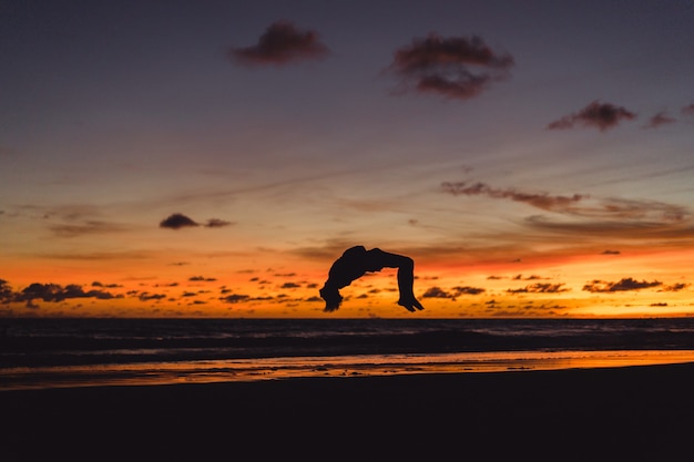 Free photo people on the shore of the ocean at sunset. man jumps against the backdrop of the setting sun.