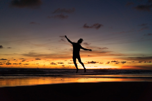 Free photo people on the shore of the ocean at sunset. man jumps