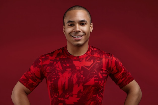 Free Photo people, style, sports and fashion concept. cropped shot of positive well set young african american male in his twenties posing in studio wearing trendy red t-shirt, looking and smiling at camera