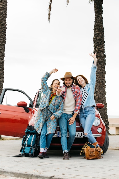 People taking selfie near red car 