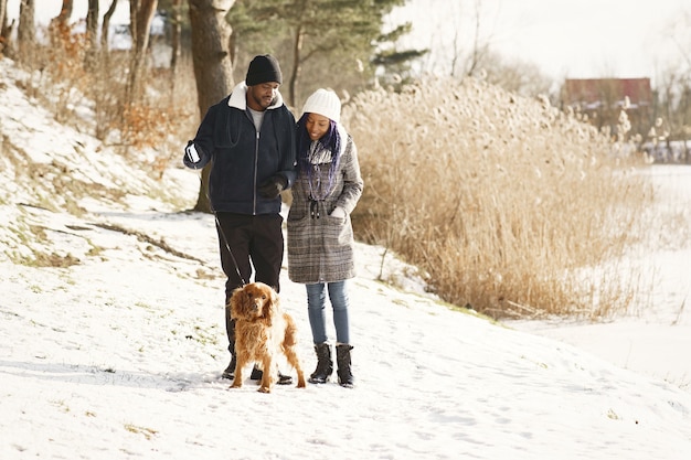 People walks outside. Winter day. African couple with dog.