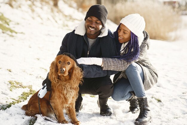 People walks outside. Winter day. African couple with dog.