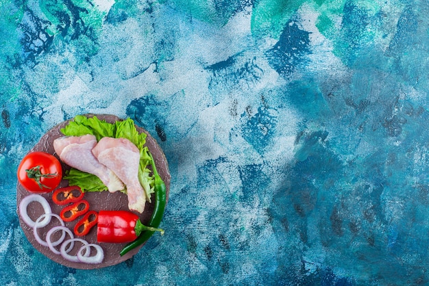 Free Photo pepper, onion rings, tomato, lettuce and chicken drumsticks on a board, on the blue background. 