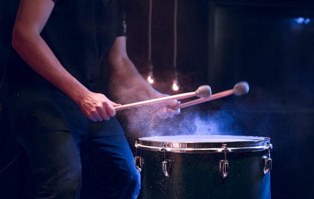 Free photo the percussionist plays with sticks on the floor tom on under studio lighting.. concert and performance concept.