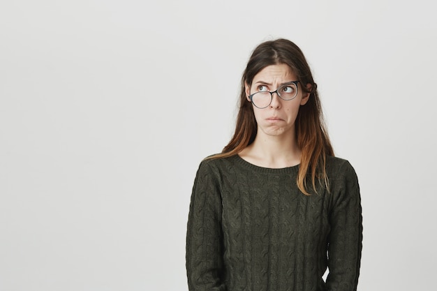 Perplexed and puzzled young woman in crooked glasses looking left troubled