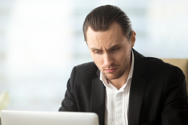 Free photo perplexed young businessman looking at laptop screen