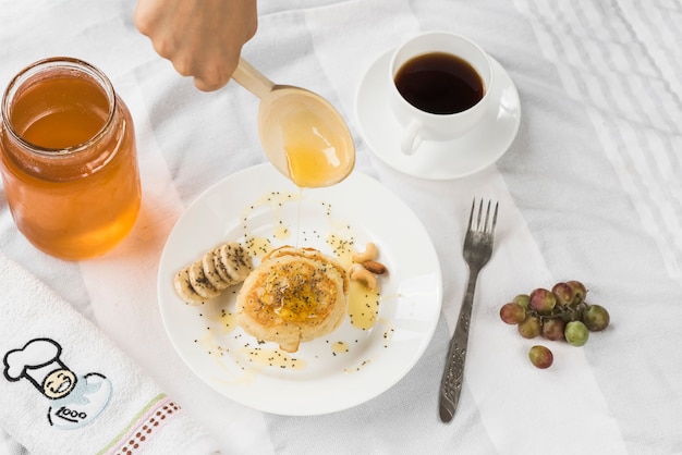 A person adding honey on pancake with wooden spoon