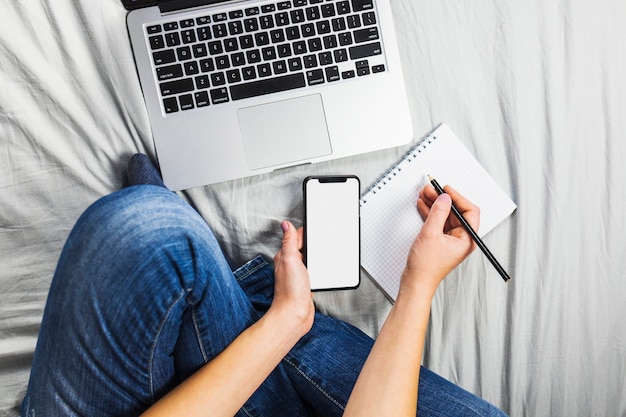 Person on bed with smartphone and notepad