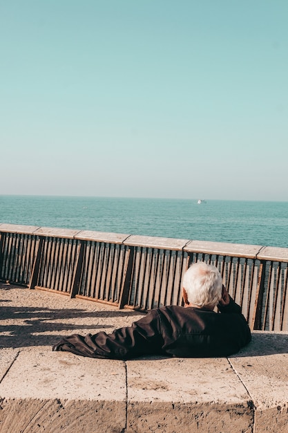 Person in black jacket sitting on brown wooden bench near sea during daytime