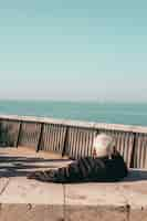 Free photo person in black jacket sitting on brown wooden bench near sea during daytime