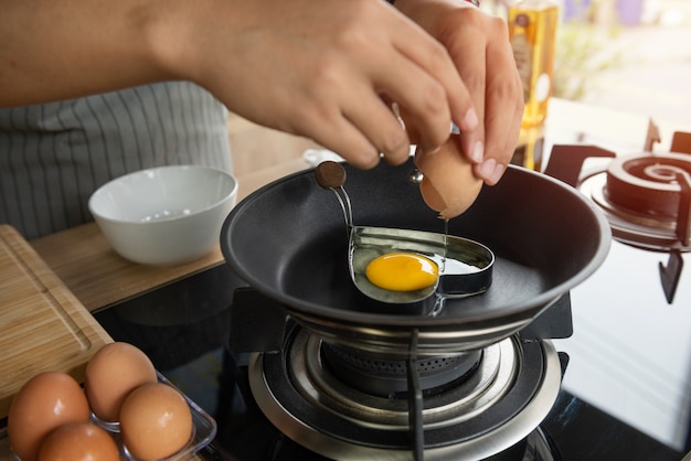 Free photo person breaking an egg into heart mold in a pan