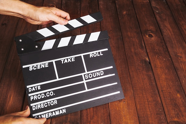 Person clapping clapperboard over wooden tabletop