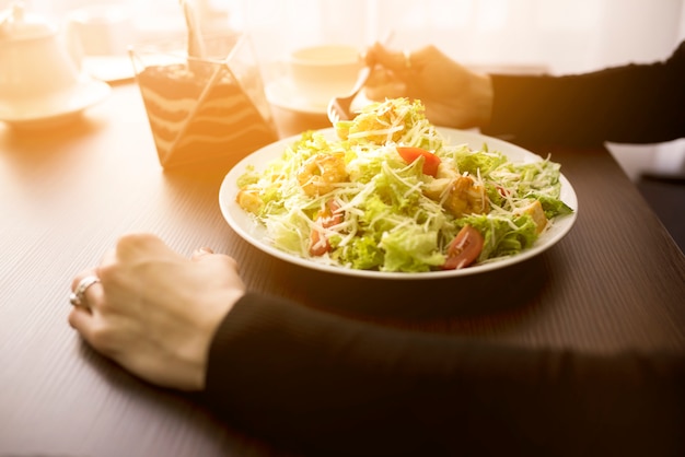 Person eating caesar salad with shrimp in restaurant