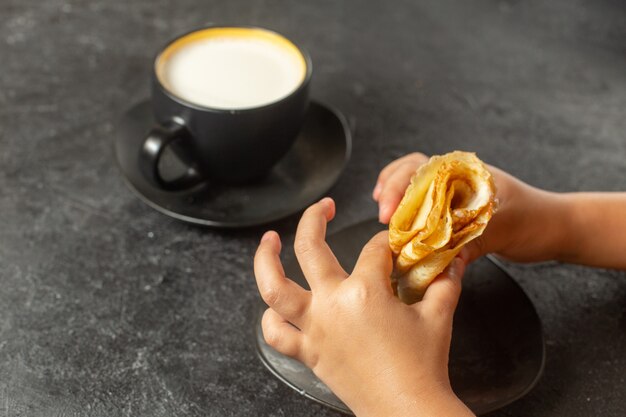 person eating pancakes rolled with cup of milk on dark