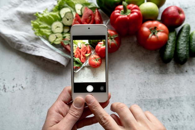 Free photo a person hand taking picture of fresh vegetable on background