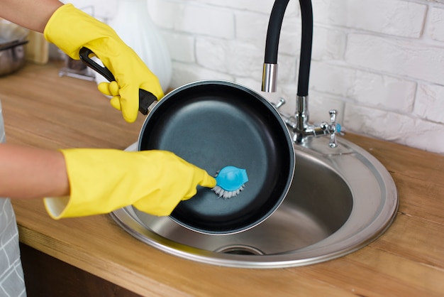 A person hand with yellow glove washing pan with brush in kitchen