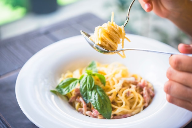 A person holding appetizing spaghetti rolled on fork