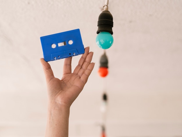 Free photo person holding blue cassette tape near multicolored light bulbs