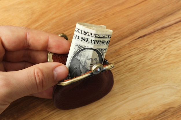 Person holding a change purse with some cash in it over a wooden surface