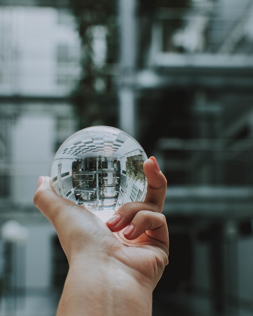 Free Photo a person holding a clear crystal glass ball with the reflection of a building