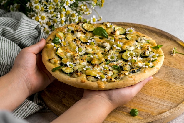 Free photo person holding delicious cooked pizza with bouquet of chamomile flowers