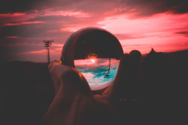 Free photo a person holding a glass ball with the reflection of colorful sky and the beautiful sunset