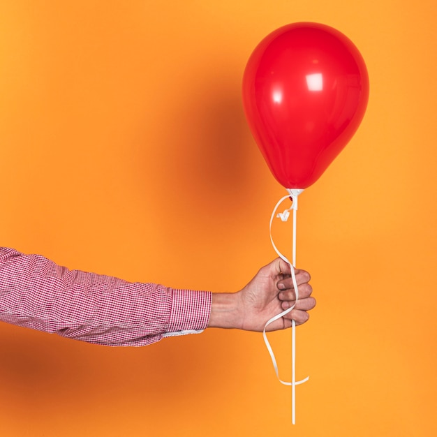 Free photo person holding a red balloon on orange background